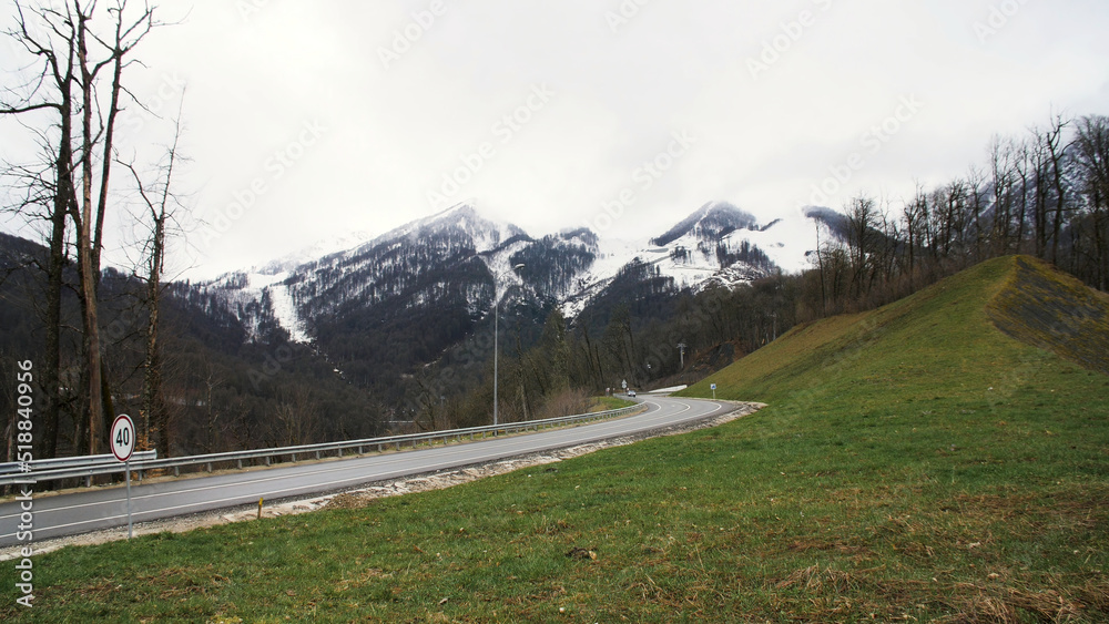 Lonely car on a mountain road turn on snowy peaks and cloudy heavy sky background. Stock footage. Mountain road car trip view.