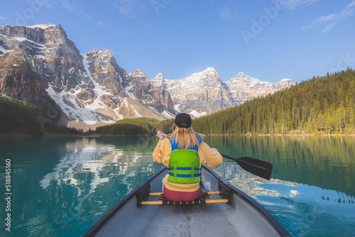 A young blonde woman paddles a canoe on the scenic, picturesque glacial Moraine Lake, a popular outdoor tourist destination in Banff National Park, Alberta, Canada in the Rocky Mountains.