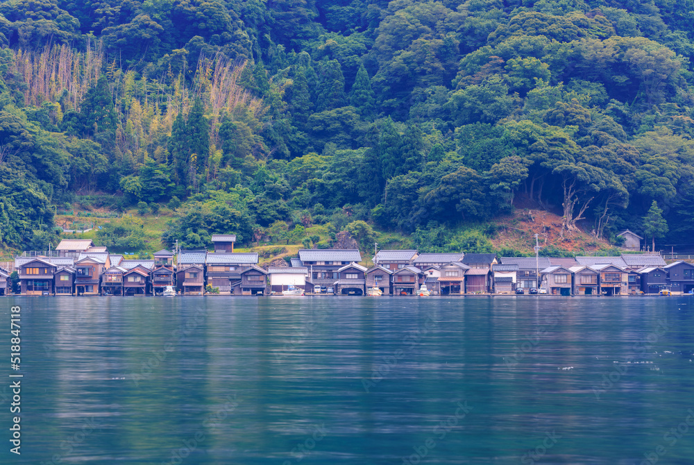 Traditional wooden boathouses line shore between calm bay and forested hills