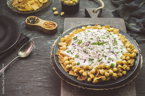 Arabic Cuisine; Lebanese authentic "Fattah" or" Fatteh" with toasted pita bread,chickpeas and yogurt sauce on rustic dark background. Close-up with copy space.