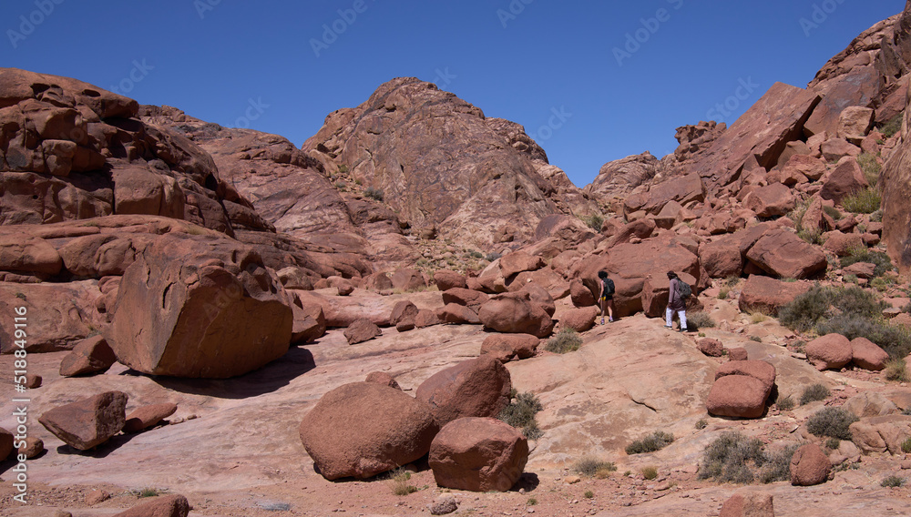 Local bedouin and female hiker on the hiking trail  in the Southern Sinai, Egypt. Panoramic view over the trail on surrounding red mountains and huge boulders.