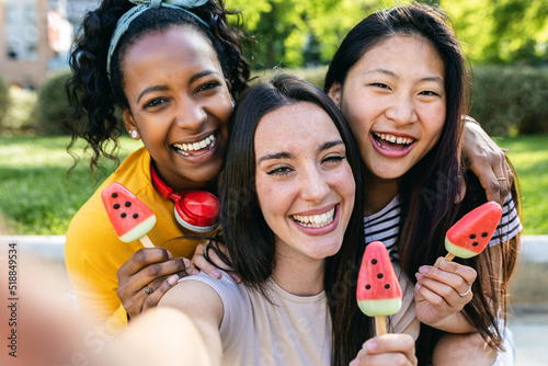 Group of three multiracial women taking selfie while eating watermelon ice cream in summer - Female friendship concept with three best millennial female friends having fun together on summer vacation photo