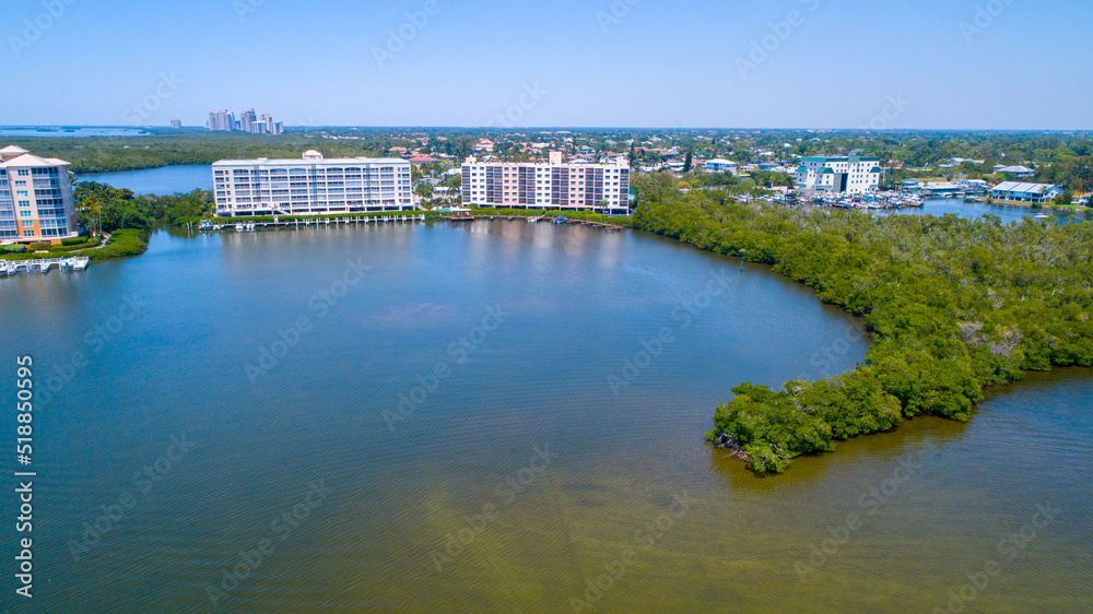 Aerial View of the Bay in Bonita Springs, Florida with Blue Water in the Foreground and Real Estate in the Background and Greenery All Around. Great Drones Eye View
