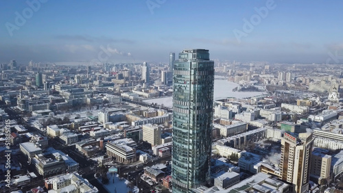 Aerial view of skyscraper is in the middle of the city in winter, blue sky sky and snowy roofs of buildings background