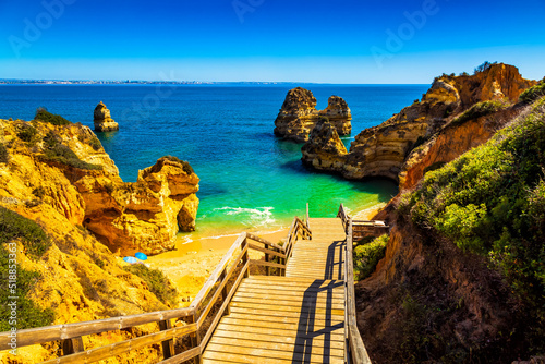 Algarve, Portugal: Wooden footbridge going down to wonderful blue ocean lagoon and Camilo beach among sandy cliffs. Praia do Camilo is located by the Atlantic Ocean neer Lagos city in Europe.