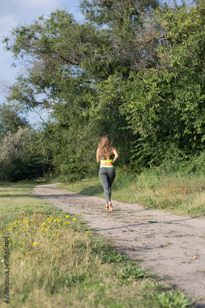 Rear view of blonde sporty woman runs in the park joggin barefoot. Running woman Rear view of blonde sporty woman runs in the park joggin barefoot. Running woman