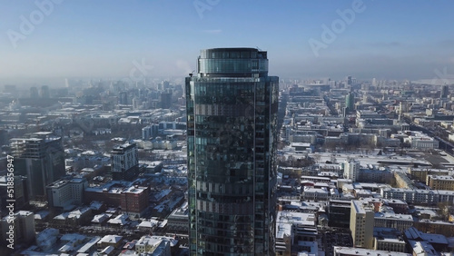 Aerial view of skyscraper is in the middle of the city in winter, blue sky sky and snowy roofs of buildings background