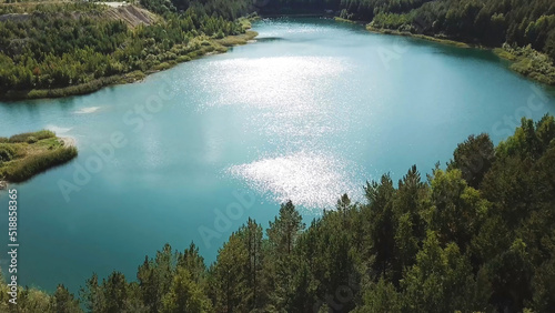 Fototapeta Naklejka Na Ścianę i Meble -  Aerial view of green forest and lake shore. Stock footage. Flying over breathtaking summer natural landscape with turquoise lake surrounded by pine tree forest.