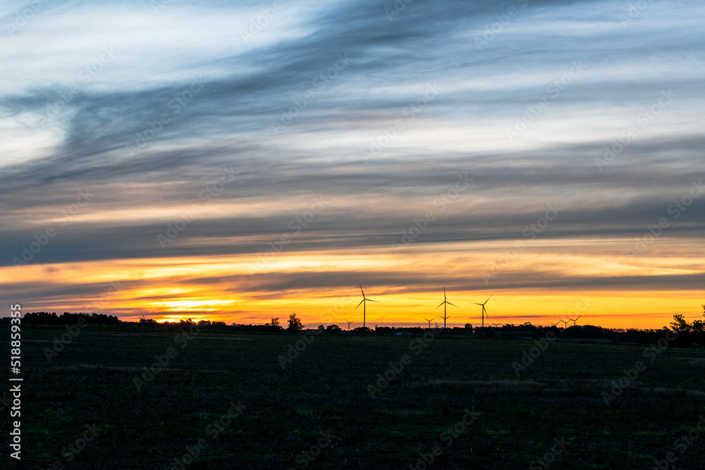 The silhouette of multiple modern windmills on the low horizon in a colorful sunset, outside of Kiyú, San José, Uruguay