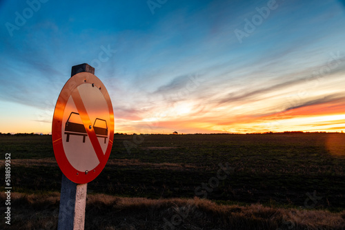 No overtaking sign on the road, under a colorful sunset, on the outskirts of Kiyú, San José, Uruguay photo