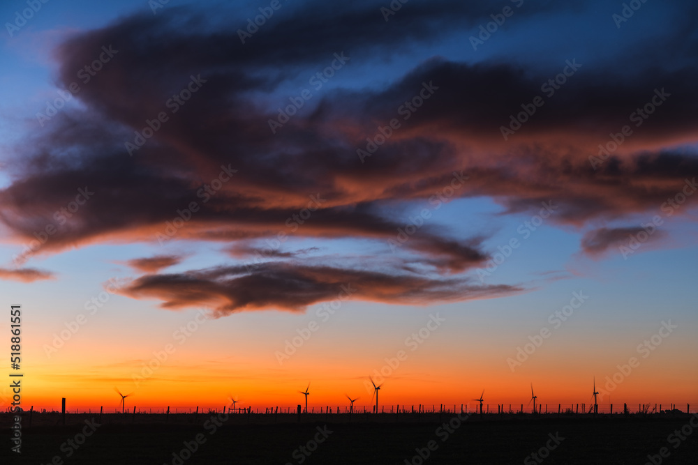 Silhouette of a set of modern windmills under a reddish sunset, with a sky with some clouds, on the outskirts of Kiyú, San José, Uruguay