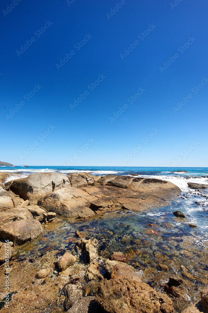 Big rocks in the ocean or sea water with a blue sky background. Beautiful landscape with a scenic view of the beach with boulders on a summer day. Relaxing scenery of the seaside or nature
