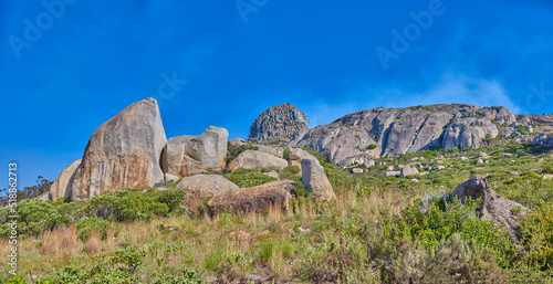 Landscape of rocky mountain with boulders against a blue sky in summer. Green field with rocks and wild grass growing on sunny day outside with copy space. Scenic remote travel destination in nature