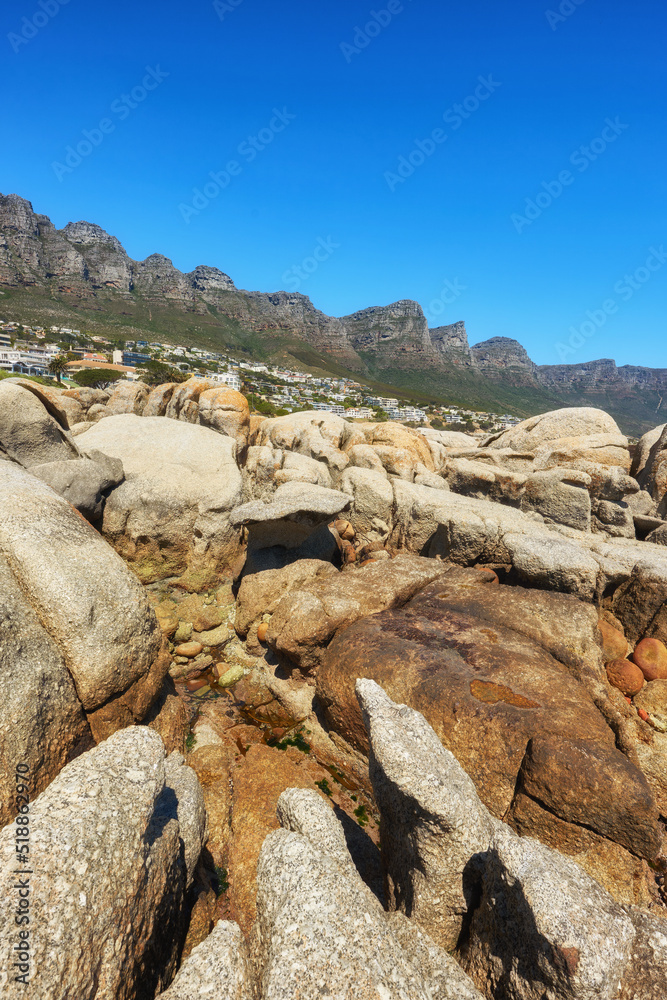 Coastal rocks with view of the mountains and city on blue sky background with copy space. Bright summer landscape of big nature stones with rough texture details near luxury houses in Cape Town