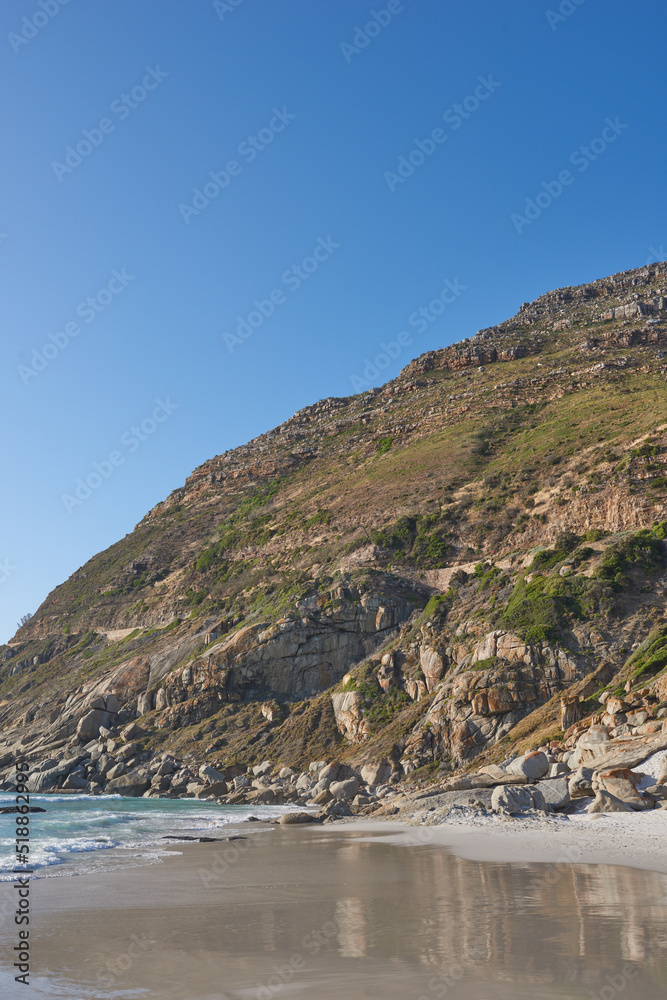 Beautiful view of a nature landscape with the sea, sand, and a blue sky background. Natural outdoors setting of the beach and green mountains. Isolated environment outside near ocean water.