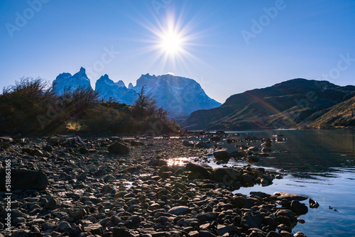 parque torres del paine, cuernos del Paine , octava maravilla del mundo, montañas, con cielo despejado azul con sol radiante y rio cristalino, orilla de rio rocoso 
