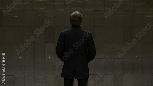 Rear view of lonely young man shot from behind at subway station add look at watch waiting for the train. Businessman at the station