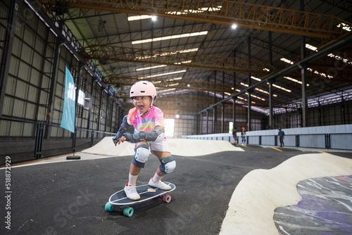 asian child or kid girl fun playing skateboard or ride surf skate in indoor pump track in skate park by extreme sports to wearing helmet elbow pads wrist and knee support for body safety on summer photo