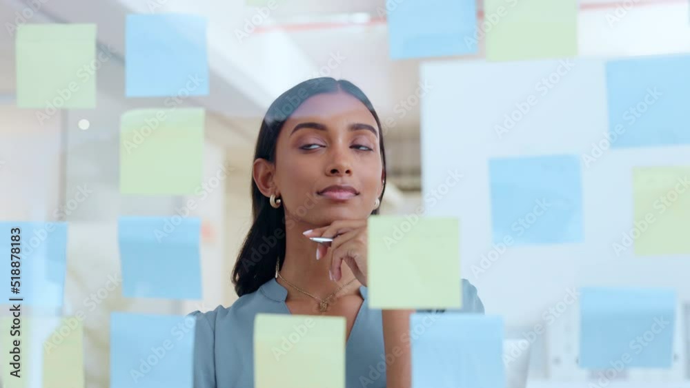 Young female notes on glass wall. Woman brainstorming, planning in a corporate setting showing leadership, management skills in the workplace. Business lady project strategy in office environment.