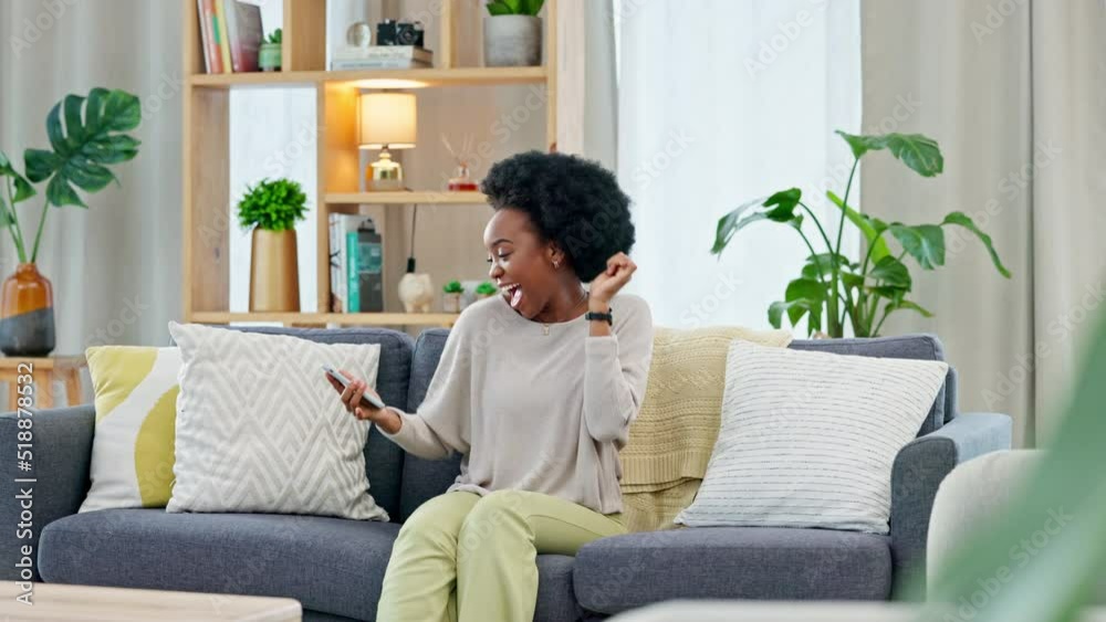 African woman celebrating a new job while sitting at home on a couch. A young females loan is approved via an email on her phone. A happy and excited lady cheering for a promotion on a sofa African woman celebrating a new job while sitting at home on a couch. A young females loan is approved via an email on her phone. A happy and excited lady cheering for a promotion on a sofa