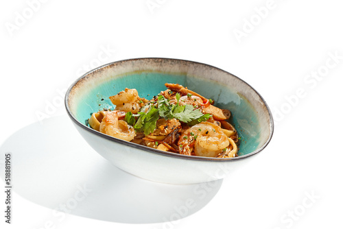 Pan asian food - udon with prawn, chicken wok on white background. Noodle with chicken and prawn in ceramic bowl. Indonesian wok with udon noodles. Spicy thai dish from noodle with shrimp and chicken.