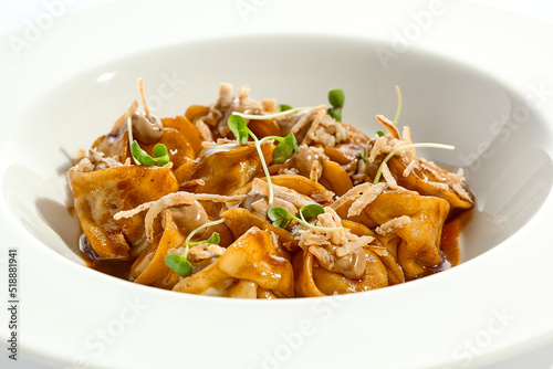 Main course in italian cuisine - meat tortellini with demi-glace sauce and mushroom cream. Beef ravioli on white plate. Tortellini with minced veal in beef sauce. Gourmet cuisine in restaurant menu.