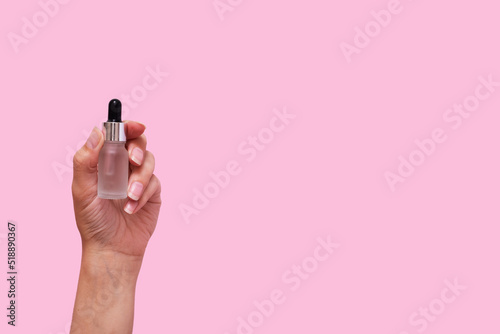 Female hand with cosmetic product in dropper bottle mock up isolated on pink color background