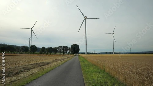 Rotating windmills in rural environment with a path, fields and some trees and bushes photo