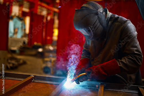 Laborer in protective mask welds manually metal frame photo