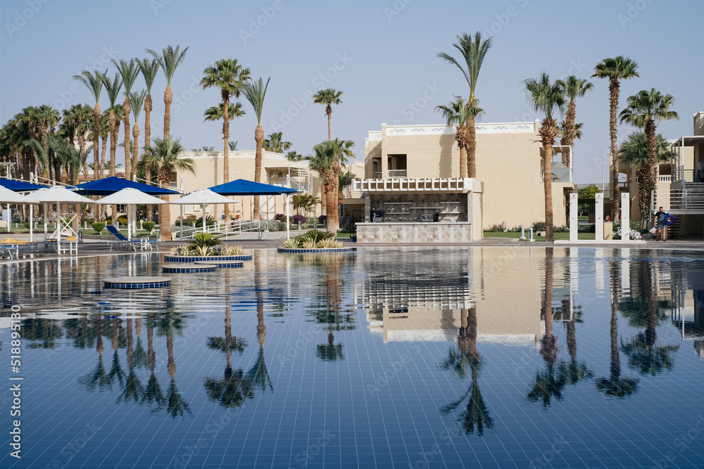 seafront with palm trees and lawn. Swimming pool by hotel with reflection. No people seafront with palm trees and lawn. Swimming pool by hotel with reflection. No people