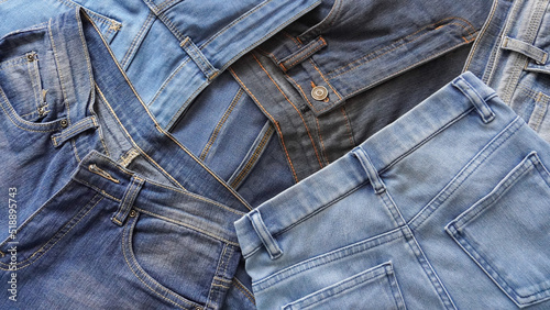 Stack of pairs of denim jeans of various blue shades and sizes