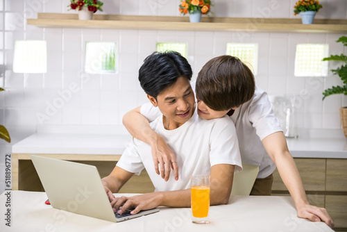 Young LGBT Asian gay man hug his partner work on computer