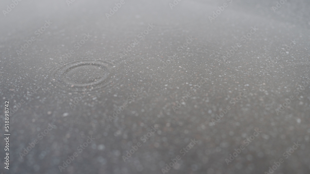 few raindrops fall in puddle on asphalt few raindrops fall in puddle on asphalt