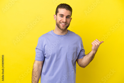 Handsome blonde man over isolated yellow background pointing to the side to present a product