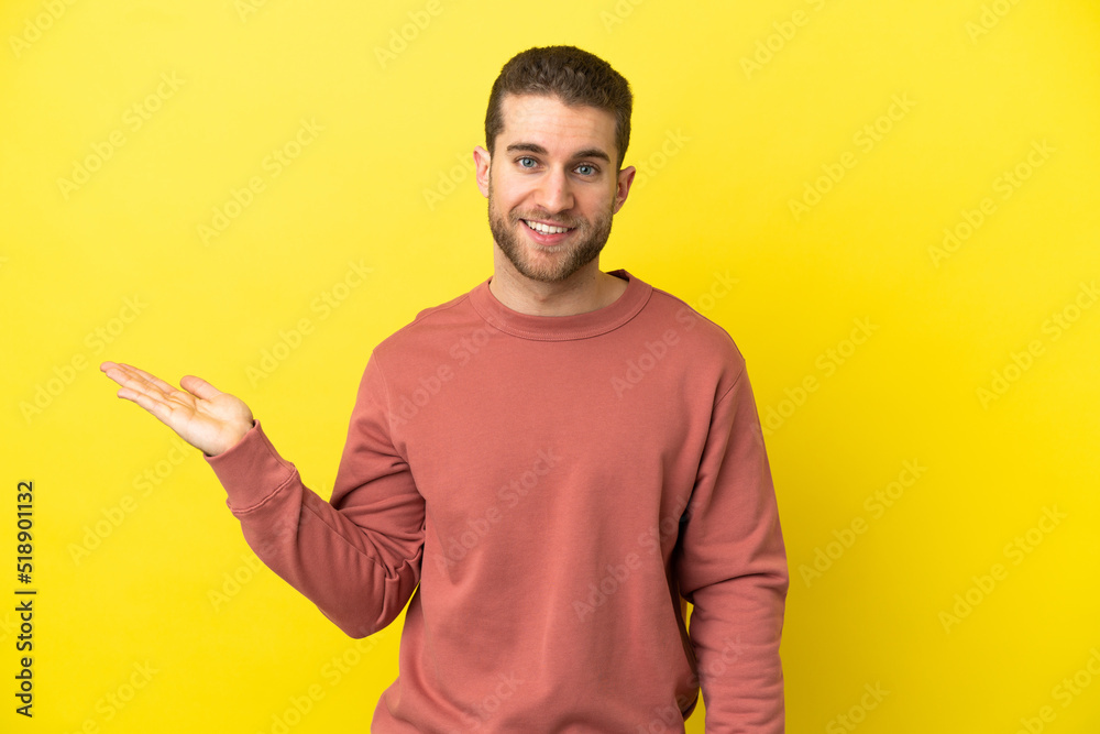 Handsome blonde man over isolated yellow background holding copyspace imaginary on the palm to insert an ad Handsome blonde man over isolated yellow background holding copyspace imaginary on the palm to insert an ad