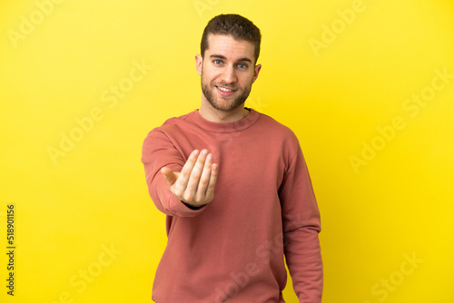 Handsome blonde man over isolated yellow background inviting to come with hand. Happy that you came © luismolinero