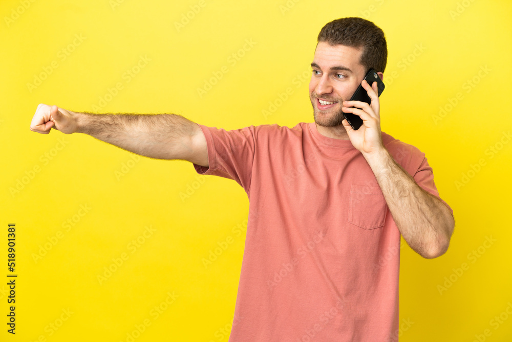 Handsome blonde man using mobile phone over isolated background giving a thumbs up gesture Handsome blonde man using mobile phone over isolated background giving a thumbs up gesture