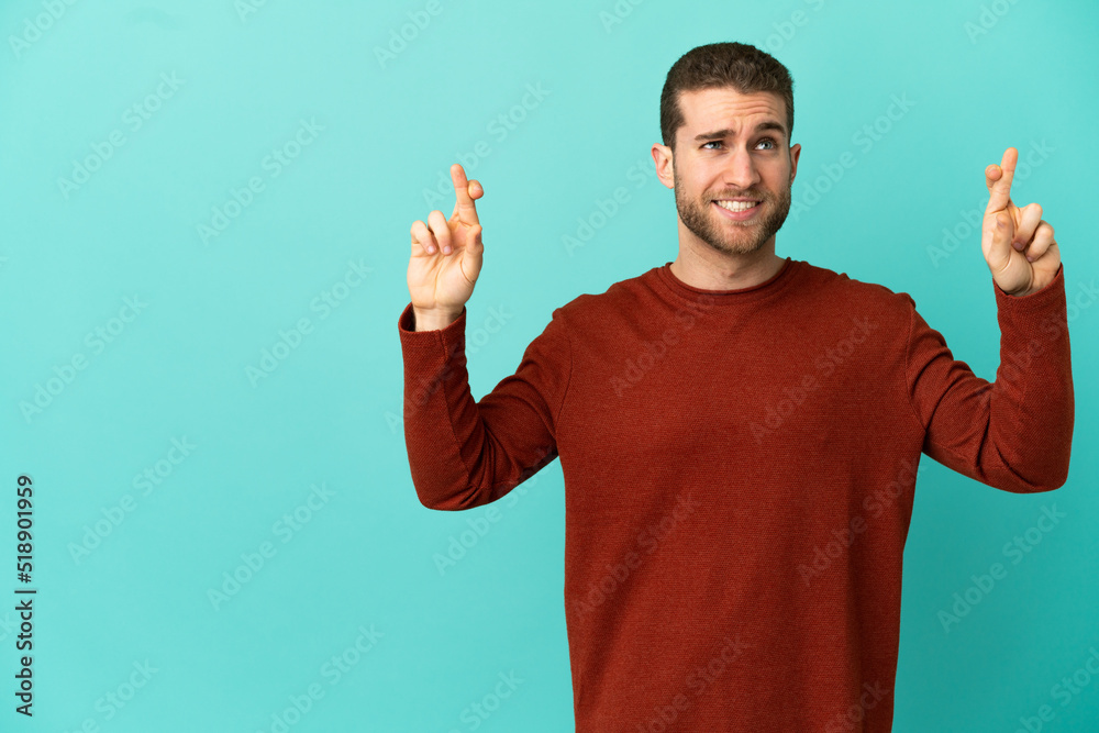 Handsome blonde man over isolated blue background with fingers crossing and wishing the best