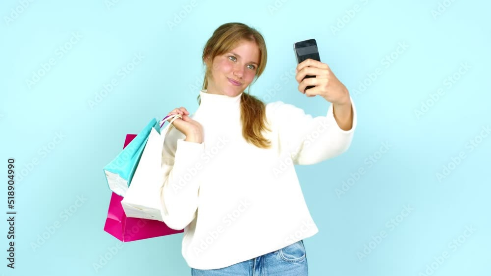 Young pretty blonde woman holding shopping bags while making a selfie isolated on background Young pretty blonde woman holding shopping bags while making a selfie isolated on background