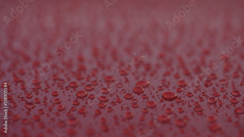 closeup shot of raindrops on red car with hydrophobic coating