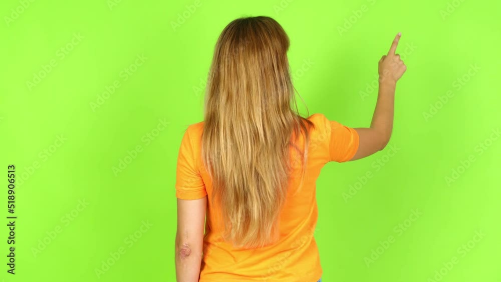 Young pretty blonde woman on green screen chroma key pointing back with the index finger over isolated background
