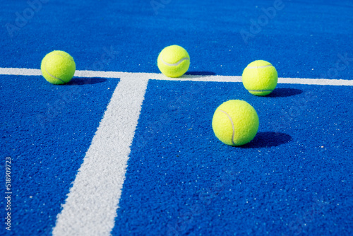 Selective focus, four paddle tennis balls on a blue paddle tennis court.
