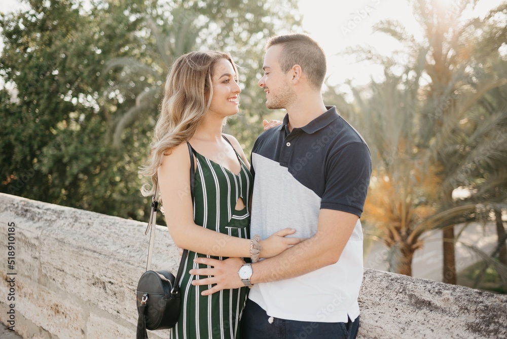 A girl in a green dress is hugging her boyfriend on the ancient bridge at the sunset in old Spain town. A couple of tourists on a date in the evening in Valencia. Romantic moment.