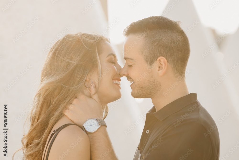 A close photo of a romantic guy who is holding his girlfriend in the modern urban space at the sunset in a Spain town. A couple of tourists on a date in the evening in Valencia.