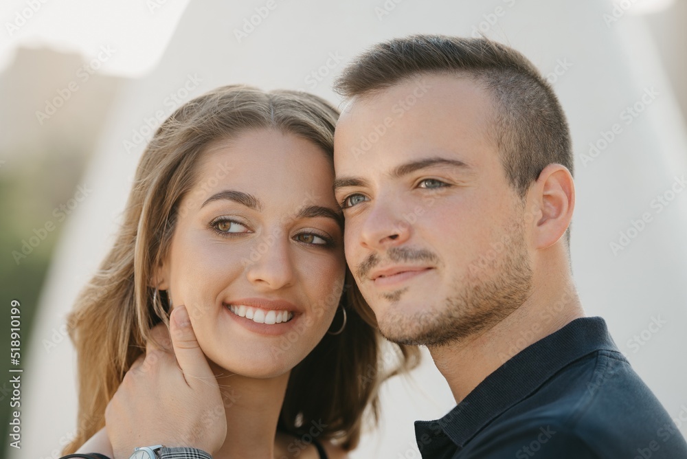 A romantic guy is holding his smiling girlfriend in the modern urban space at the sunset in a Spain town. A couple of tourists on a date in the evening in Valencia.