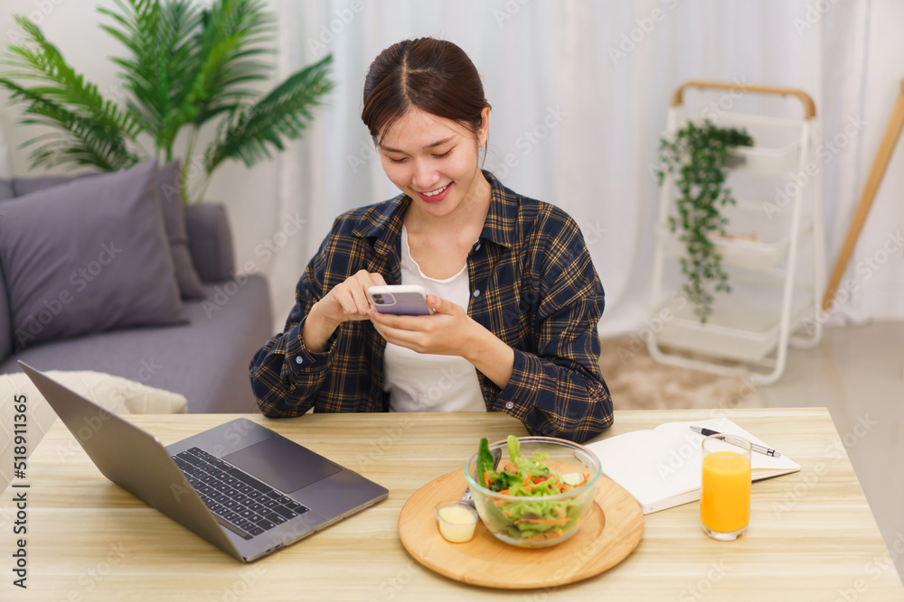 Lifestyle in living room concept, Young Asian woman using smartphone and eating vegetable salad Lifestyle in living room concept, Young Asian woman using smartphone and eating vegetable salad
