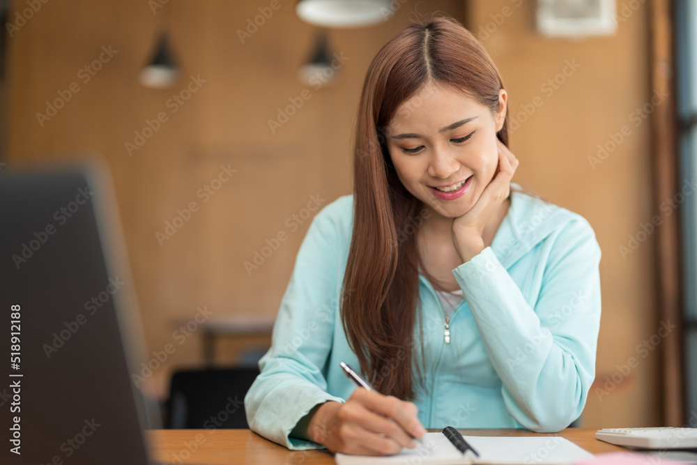 College education concept, Teenage girl watching video tutorial of tutor on laptop and taking notes College education concept, Teenage girl watching video tutorial of tutor on laptop and taking notes