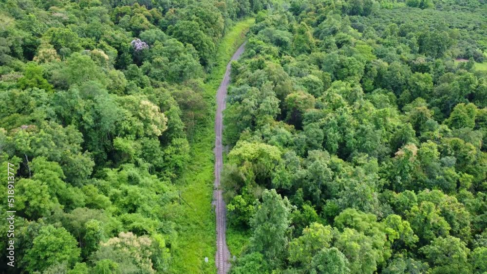 Aerial view of a drone on a railway track in a rural landscape with green forest during the rainy season. The drone flew above the forest and saw the railroad tracks in the distance. Aerial view of a drone on a railway track in a rural landscape with green forest during the rainy season. The drone flew above the forest and saw the railroad tracks in the distance.