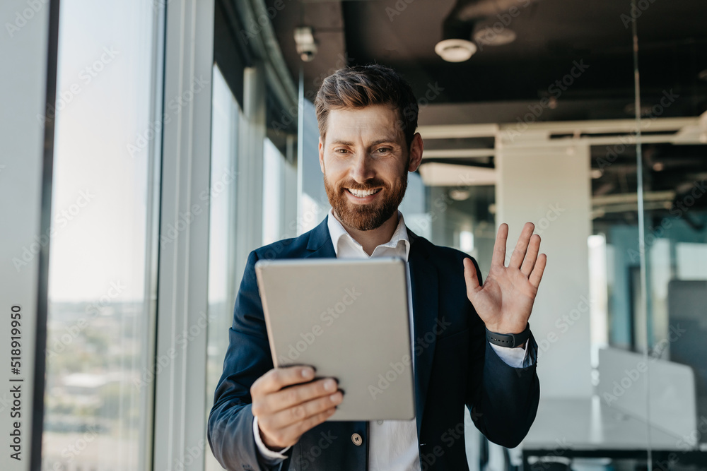 Happy caucasian businessman in suit working in office, having video chat with business partners via digital tablet Happy caucasian businessman in suit working in office, having video chat with business partners via digital tablet