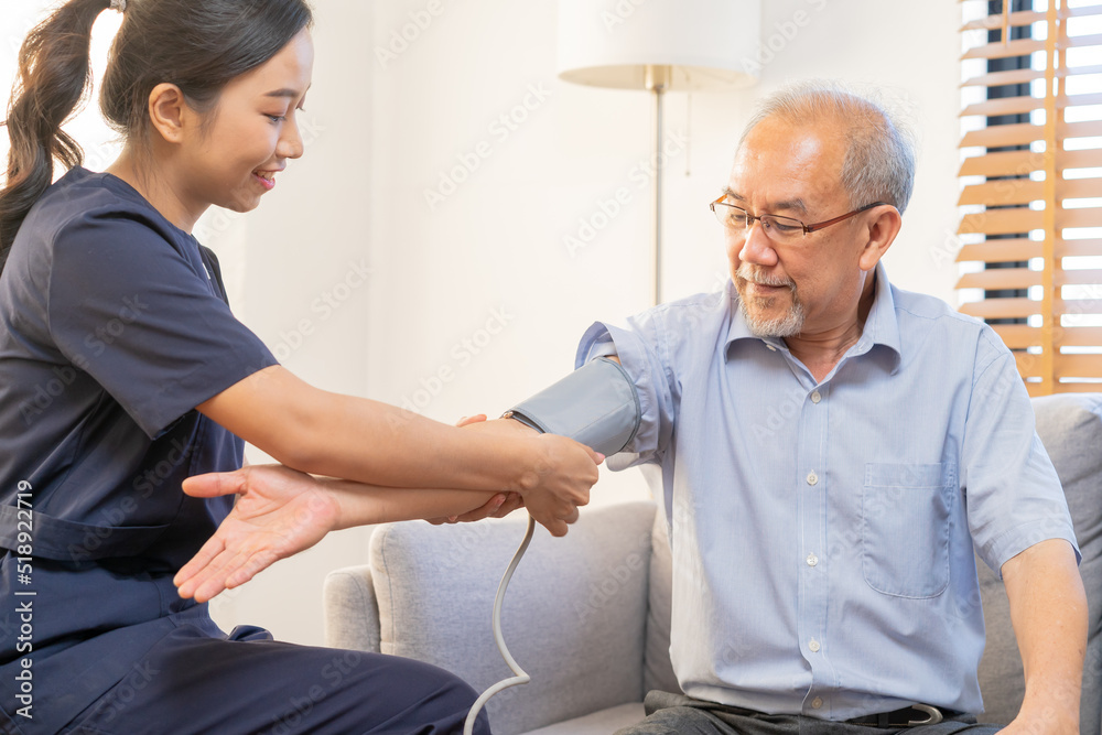 Obraz premium Pressure measurement of hypertension in elderly man sitting on couch, young woman nurse or caregiver care checking, measuring heart, blood by using sphygmomanometer monitor at home after retirement.